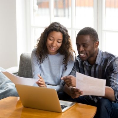 Woman and man sitting on sofa holding documents infront of a laptop